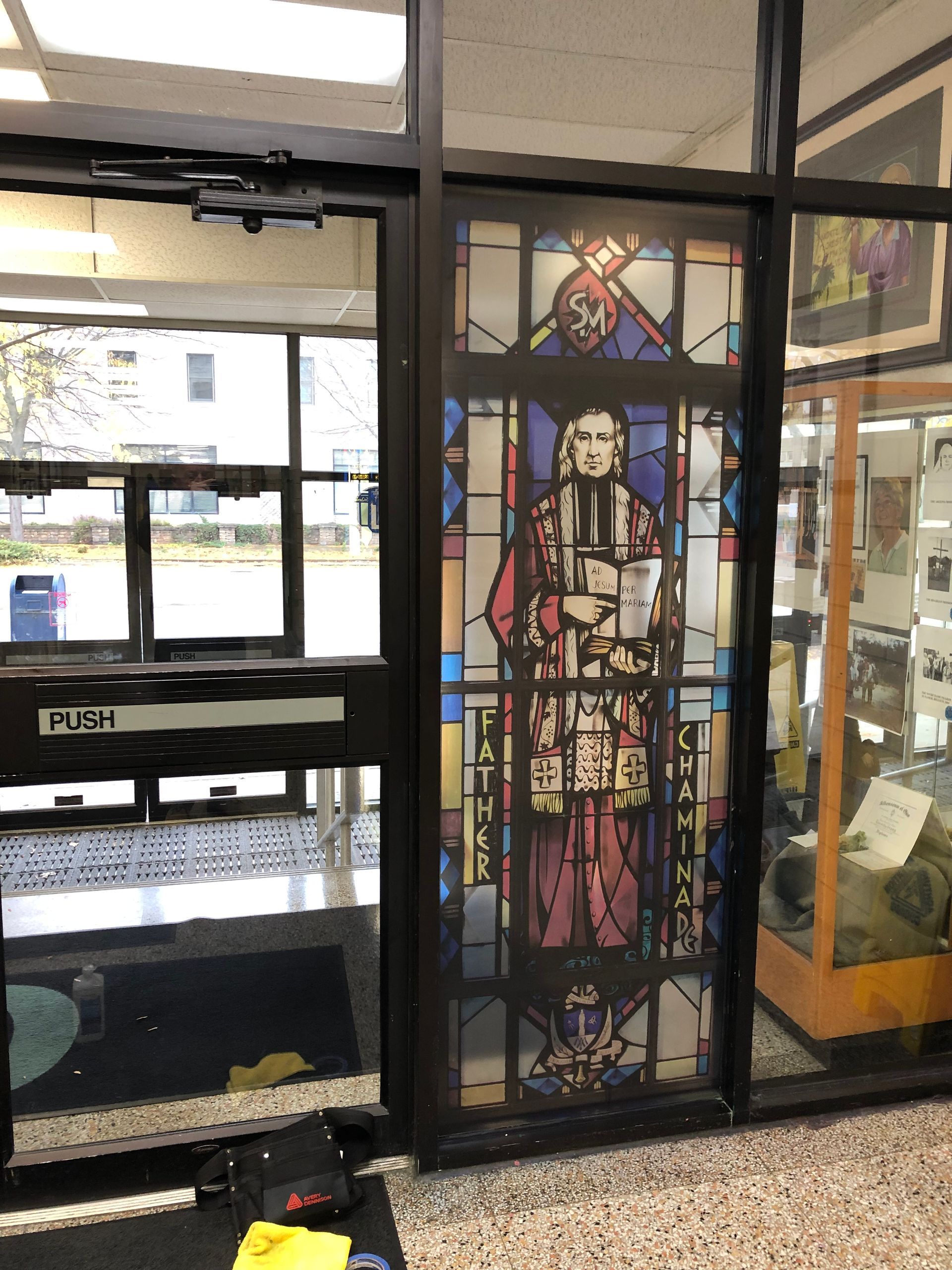 Stained glass window with a religious figure wearing red robes in a doorway.