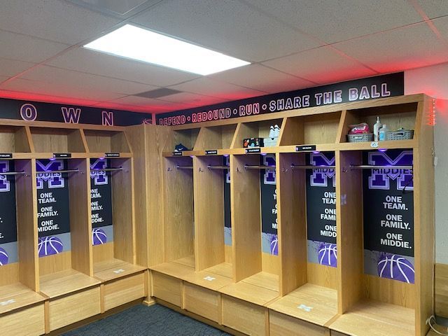 Basketball team locker room with wooden lockers, purple logos, and motivational phrases.