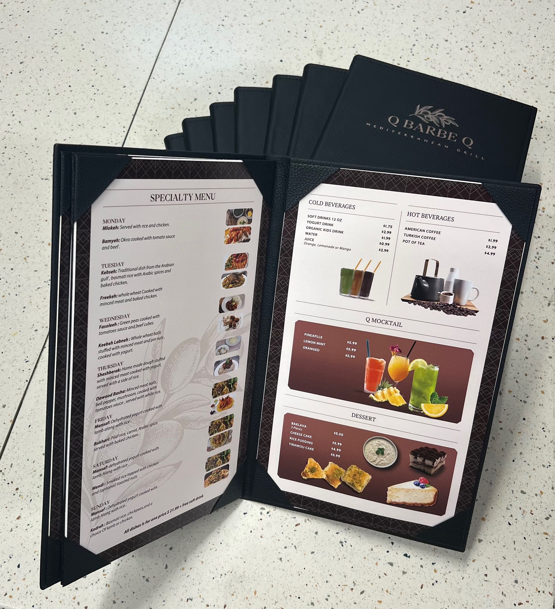 Open restaurant menu; leather-bound with food/drink options displayed, with several menus stacked in background.