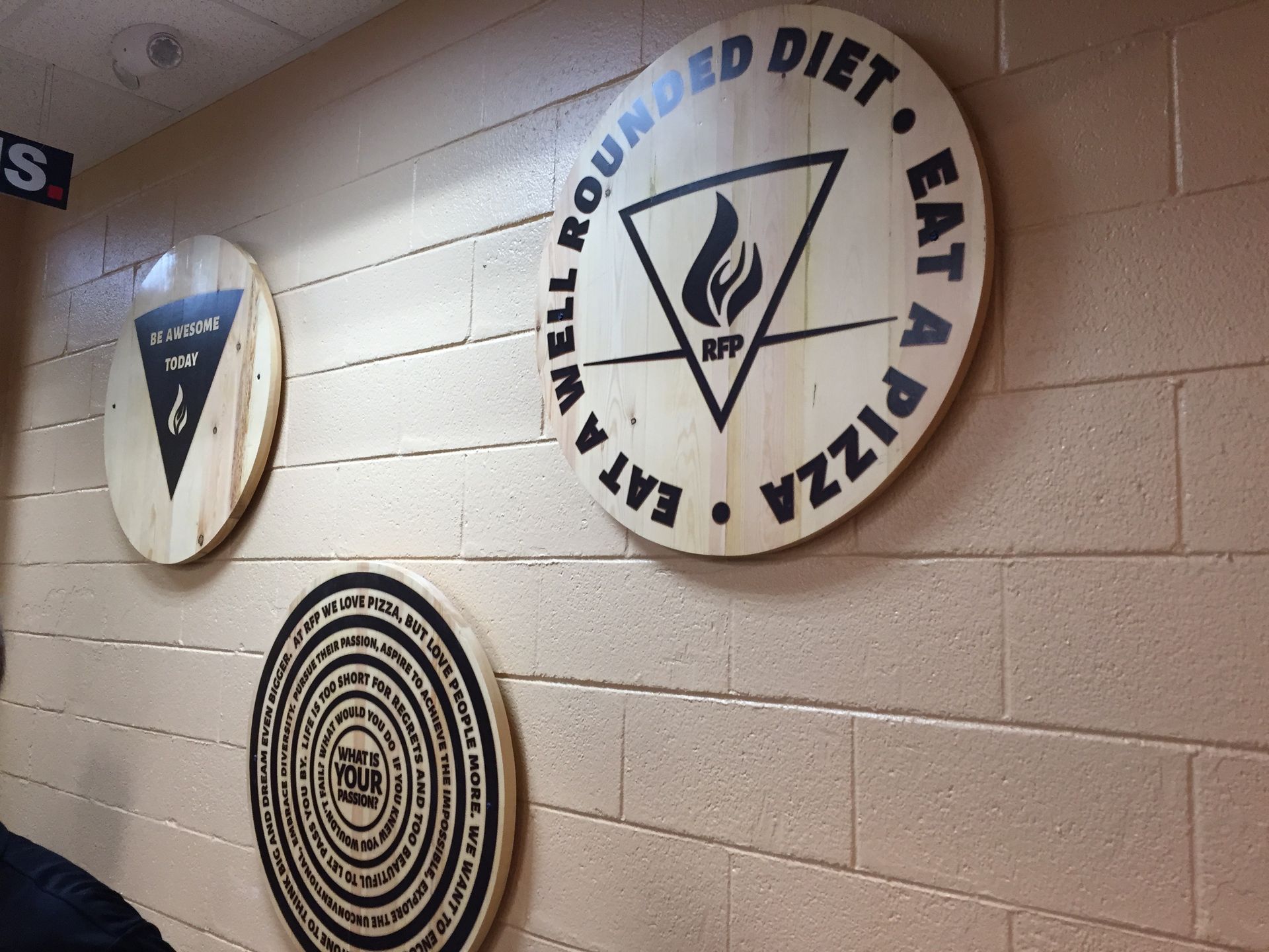 Three wooden signs on a beige wall: circular with text, a triangle with a logo, and a spiral.