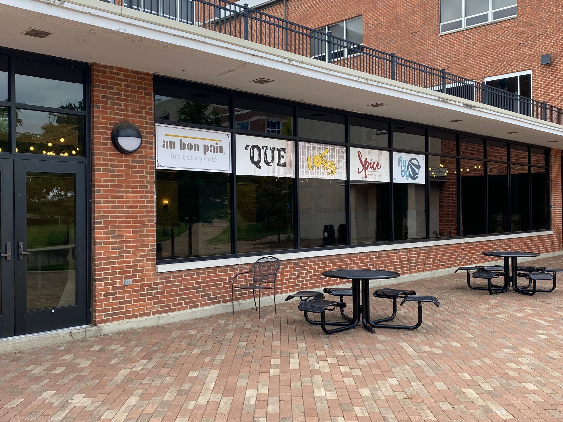 Exterior of a brick building with large windows, several signs, and picnic tables on a patio.