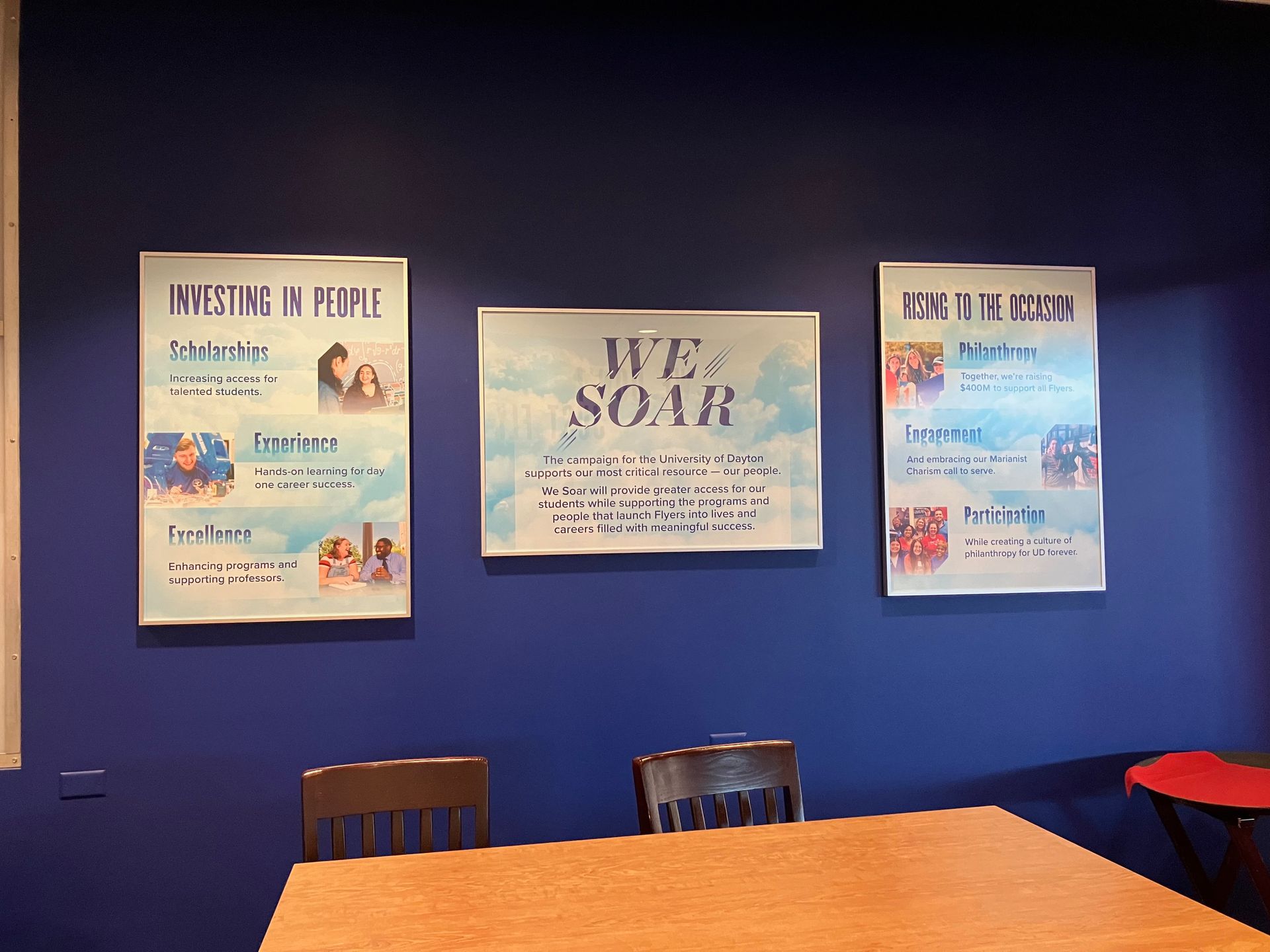 Three posters on a blue wall above a table and chairs. The central poster reads