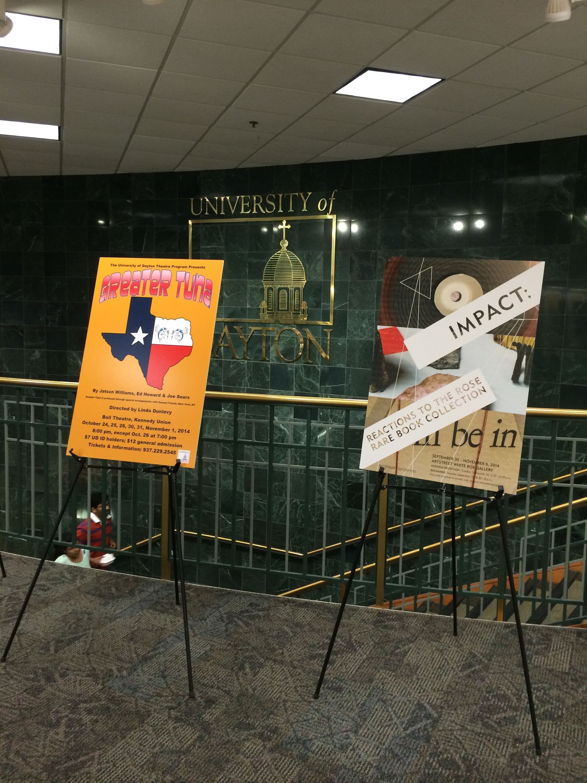 Two posters on easels, one with Texas outline, the other with plane, both in front of a building facade.