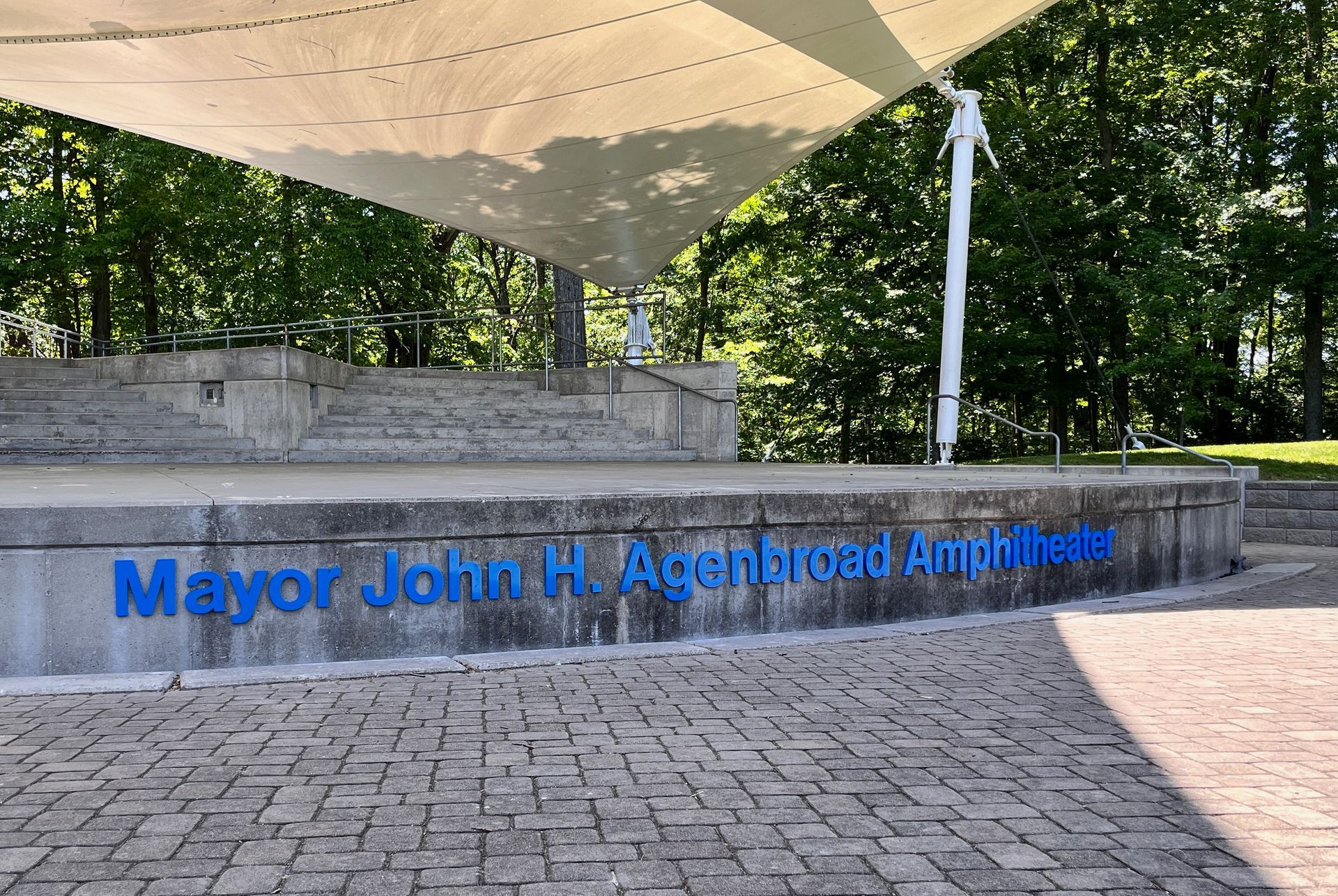 An outdoor amphitheater with a stage, canopy, and blue text: 