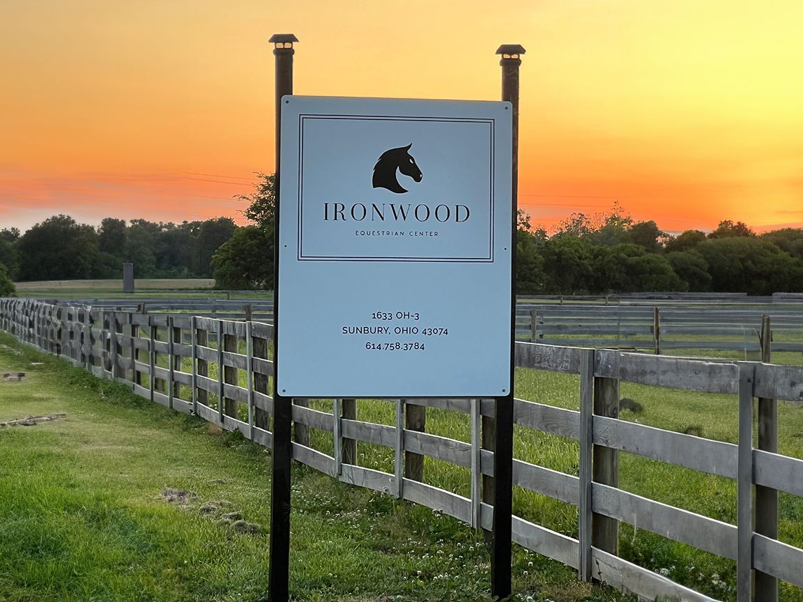 Sign for a horse farm at sunset, with a horse head silhouette logo.