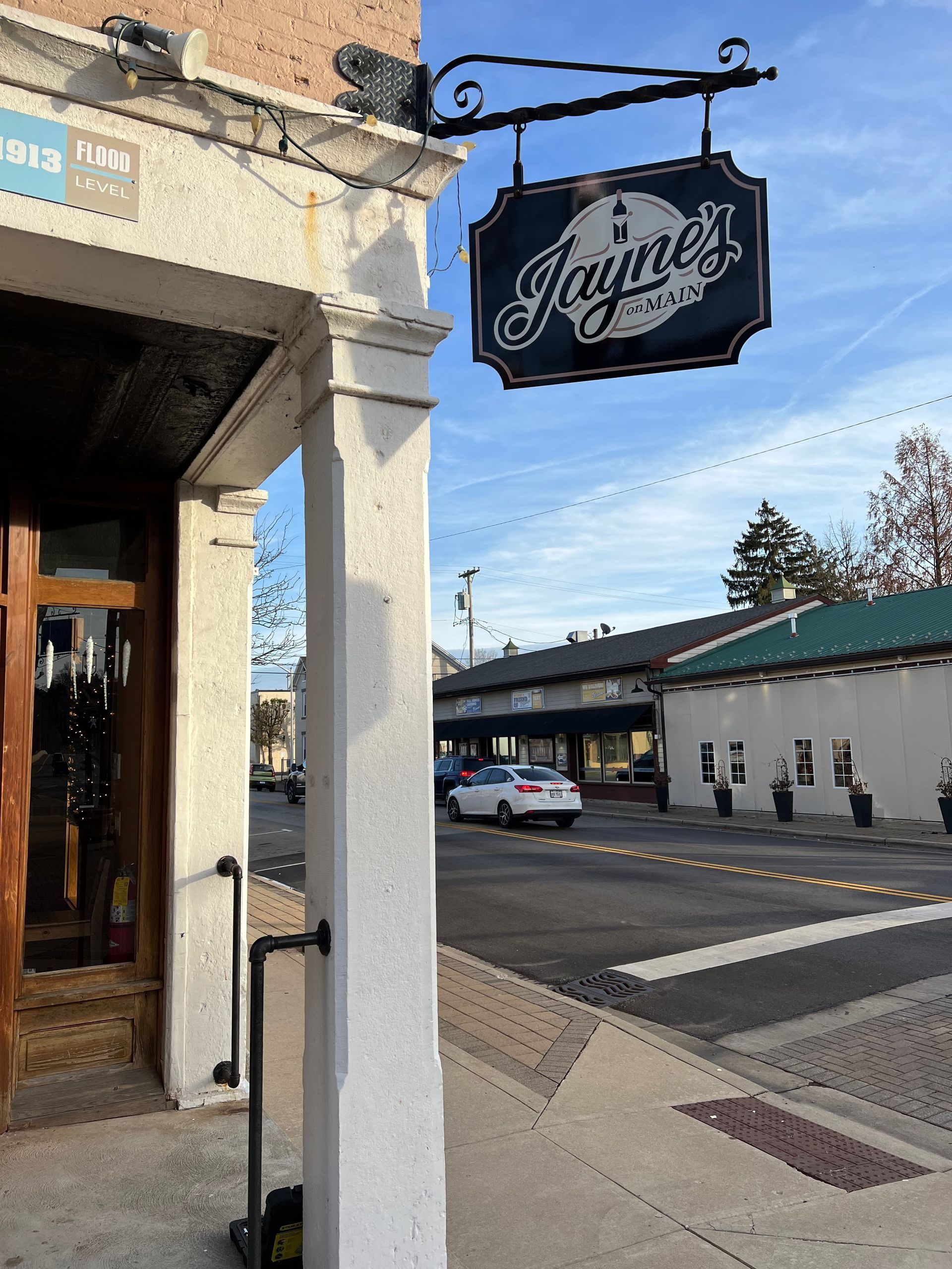 Jayne's Pizza sign hangs over a storefront on a street corner. Building with white column and a car.
