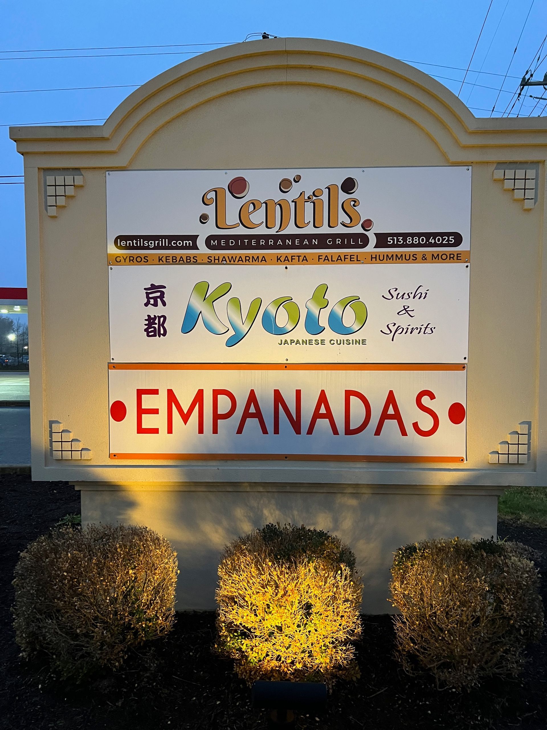 Sign for Lentil's, Kyoto, and Empanadas restaurants, beige with illuminated bushes in front.