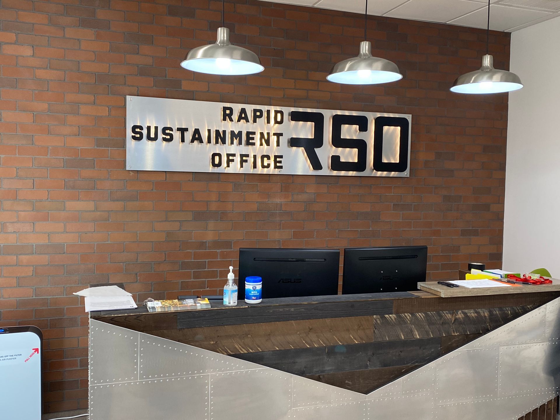 Reception desk in the Rapid Sustainment Office with a brick wall and silver pendant lights.