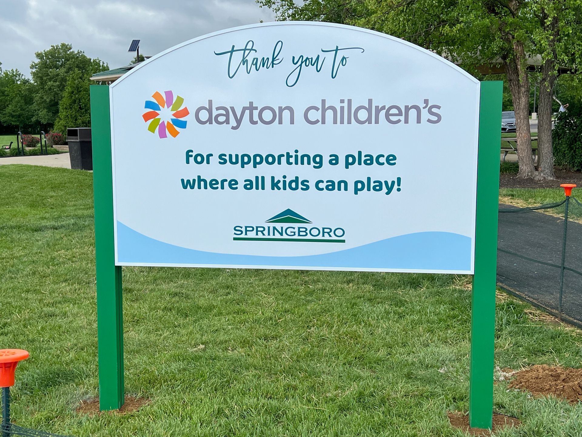 Sign thanking Dayton Children's for supporting a place for kids to play in Springboro; green posts, white sign.