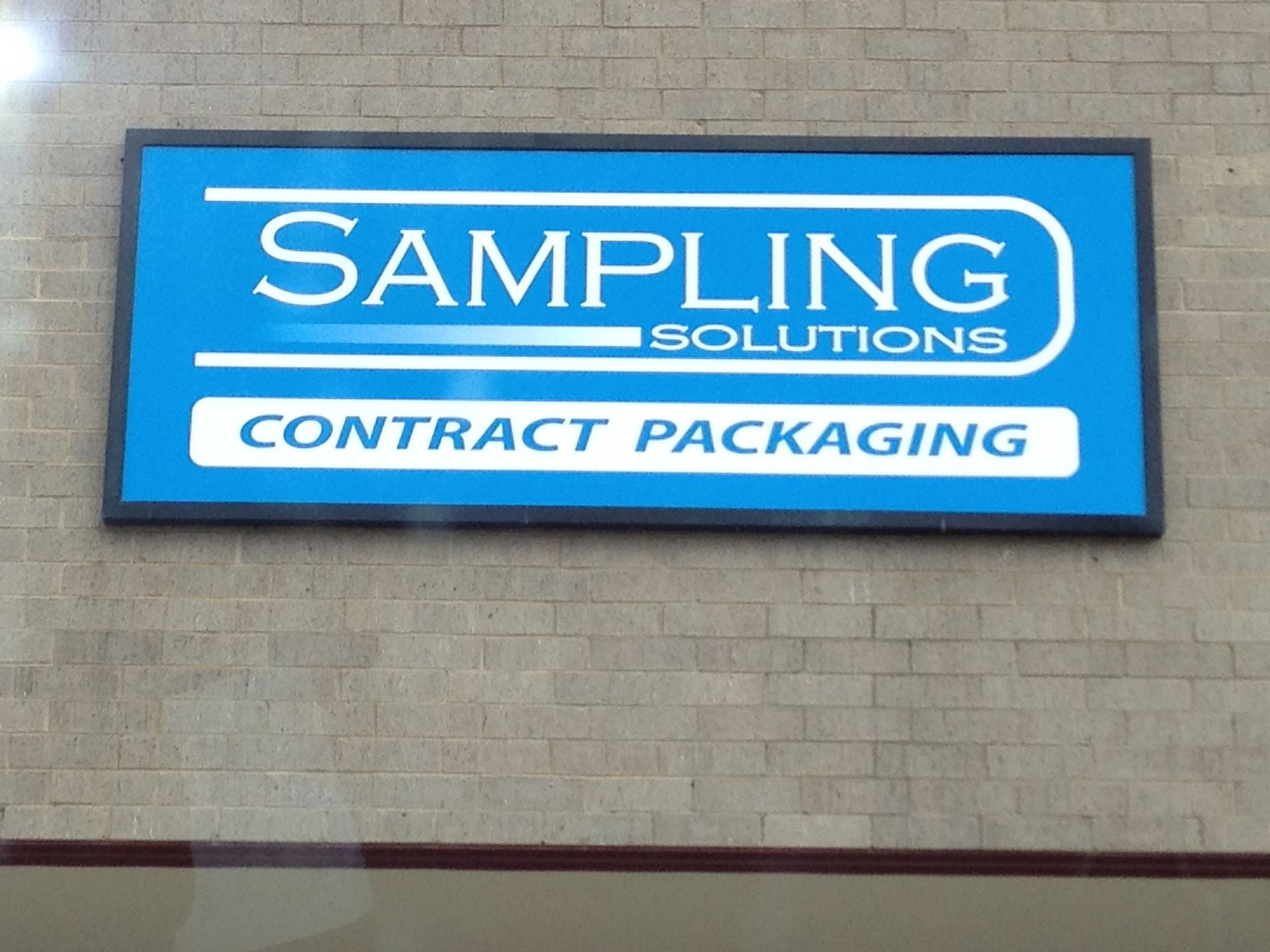 Sign for Sampling Solutions, a contract packaging company. Blue and white text on a blue background.