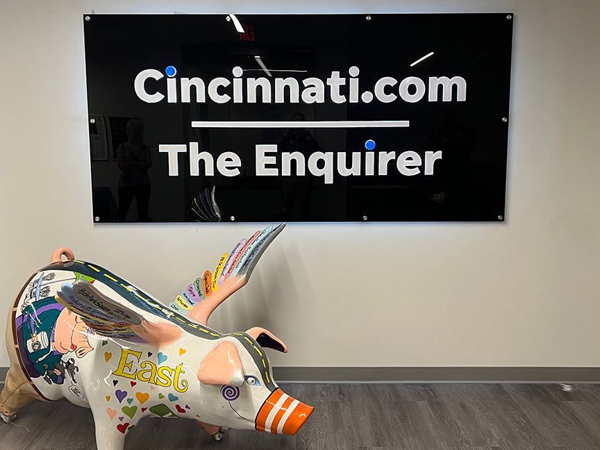Sign for Cincinnati.com and The Enquirer over a decorated pig statue, in an office.