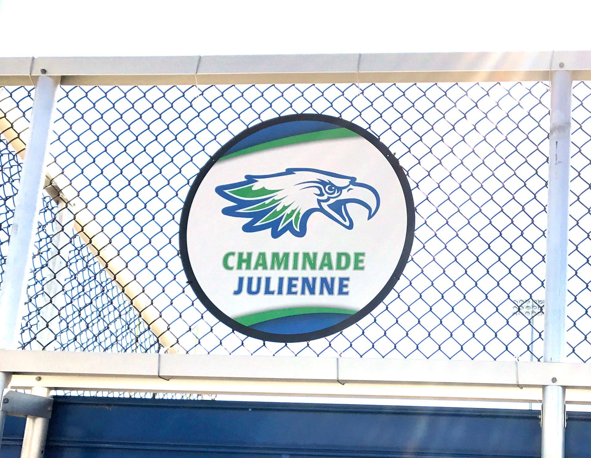 Chaminade Julienne logo on a fence. Eagle head in green and blue circle.