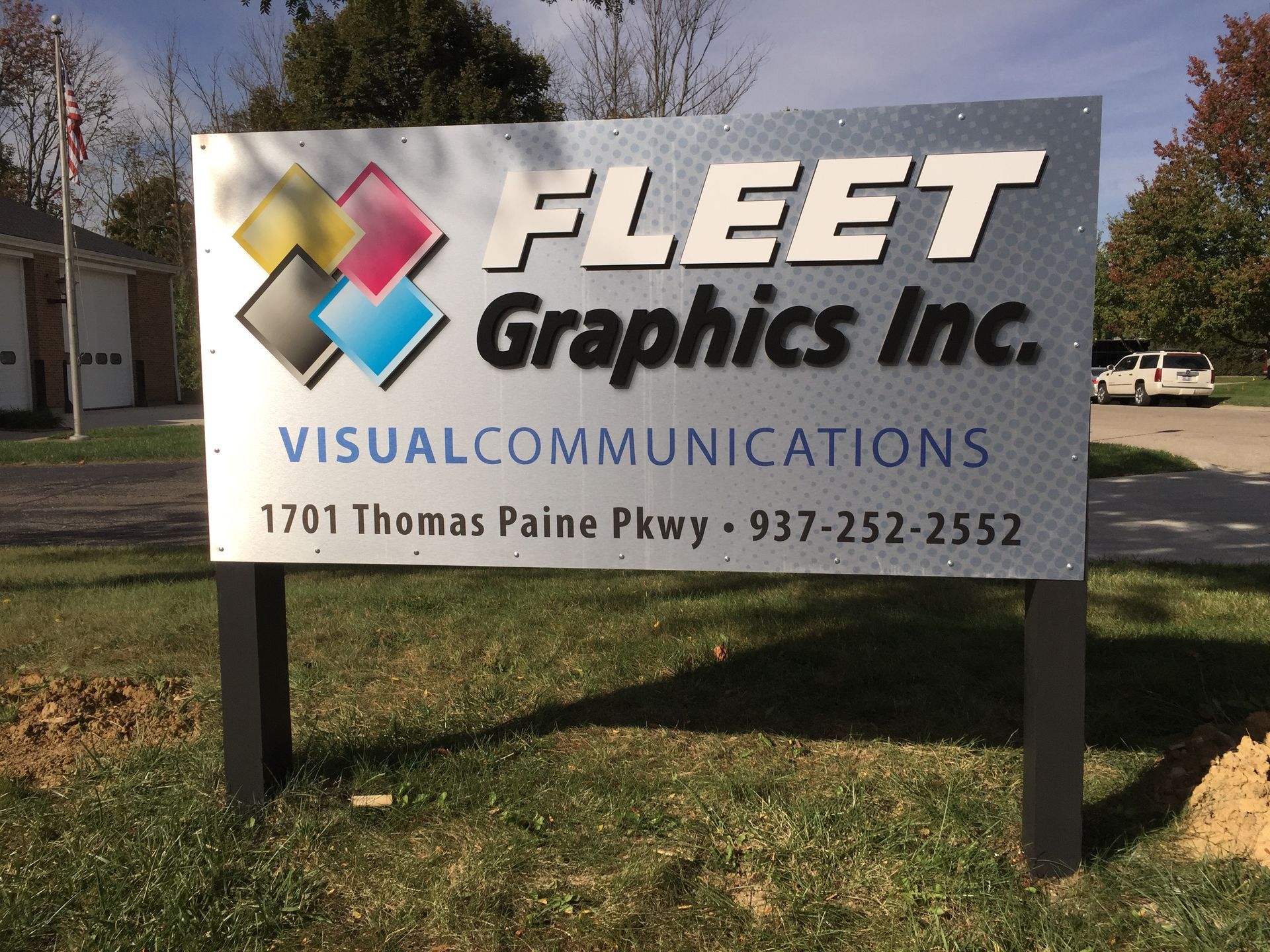 Sign for Fleet Graphics Inc. showing logo, address, and phone number, in front of a building.