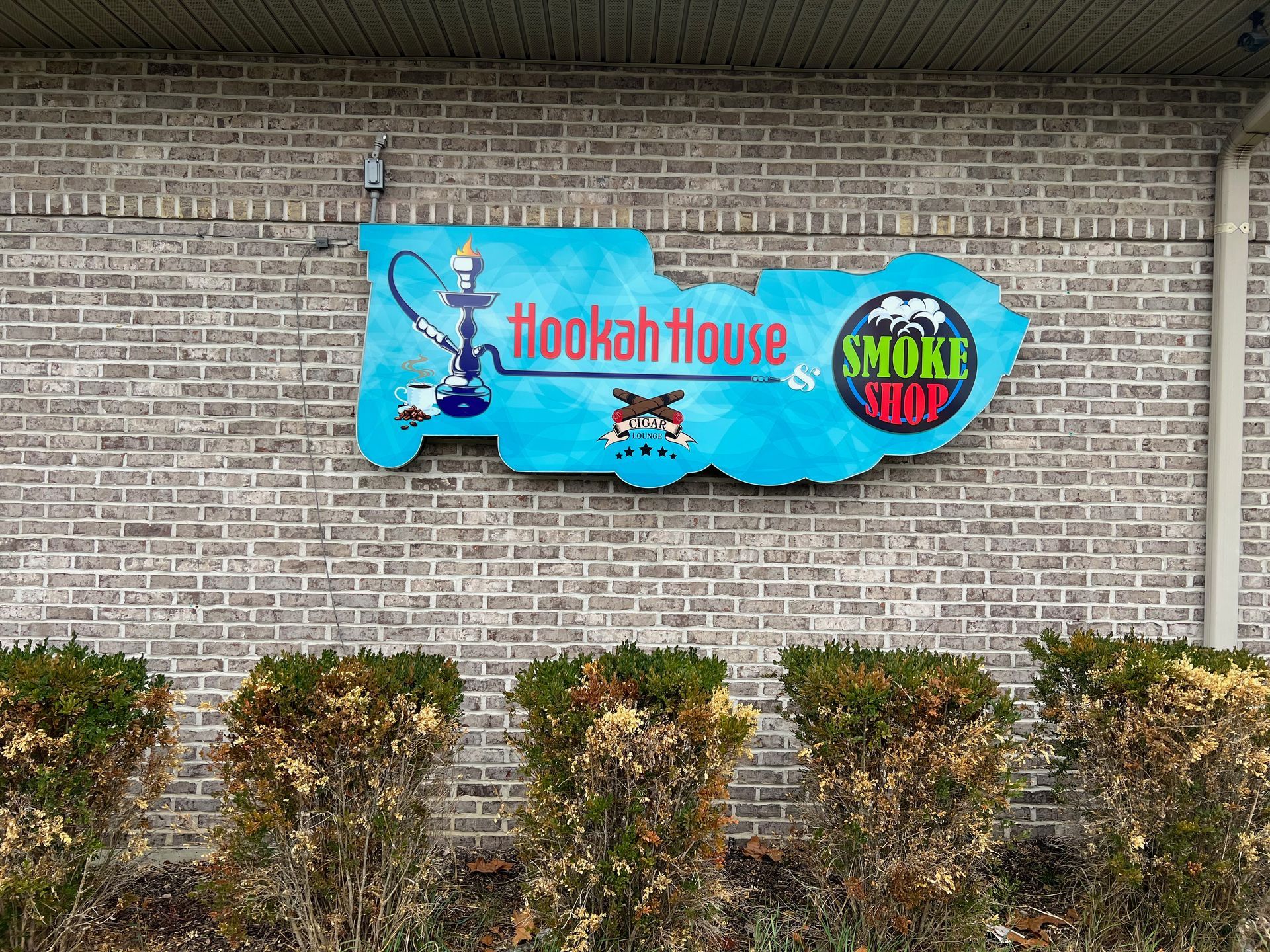 Sign for Hookah House Smoke Shop, featuring a blue, hookah-shaped sign on a brick building.