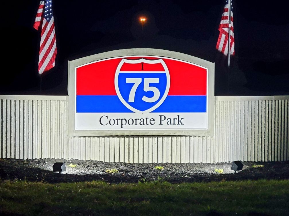Sign for I-75 Corporate Park with US flags at night.
