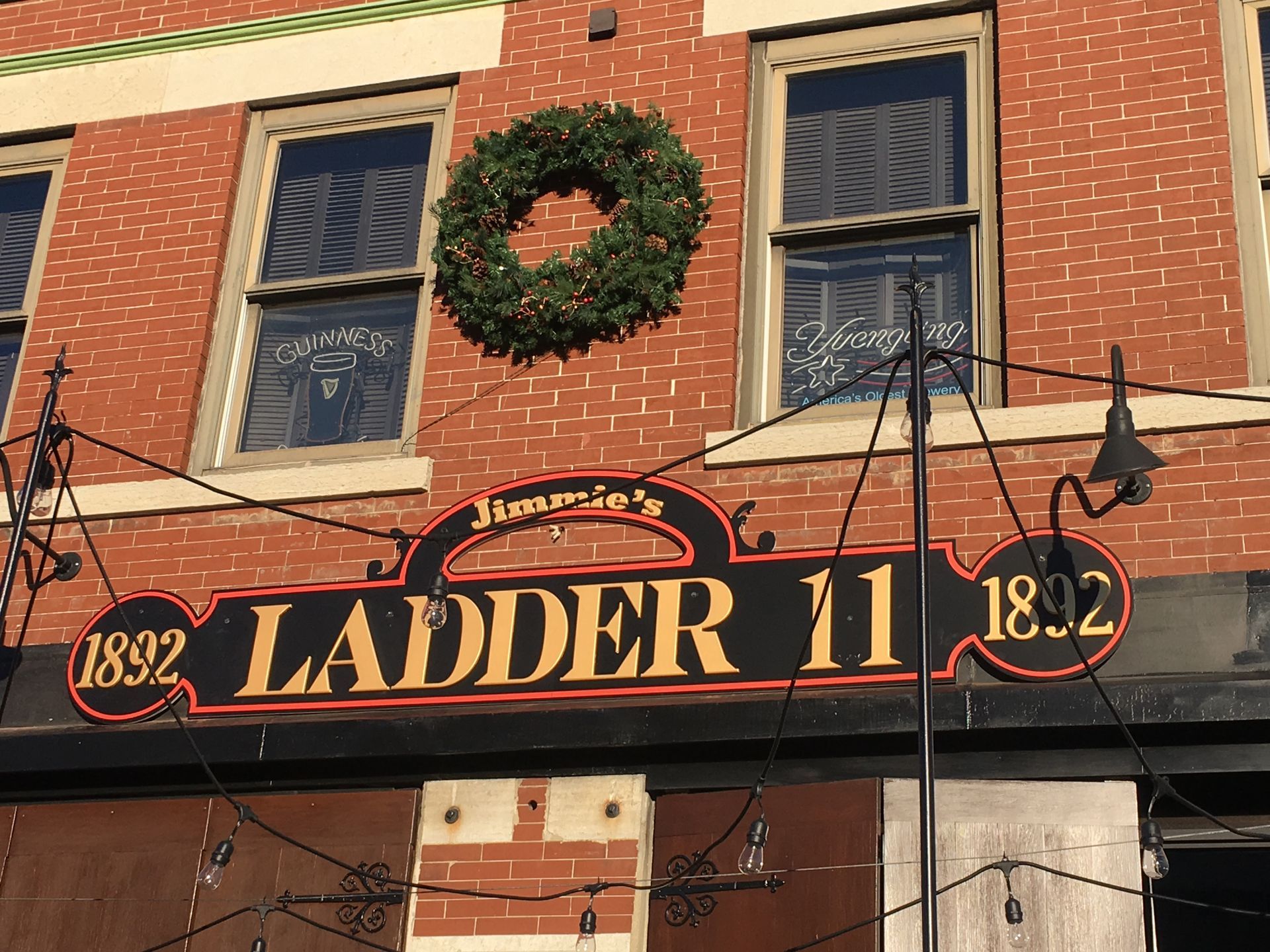 Exterior of Jimmy's Ladder 11, a bar, with a green wreath and the year 1892 on the sign.