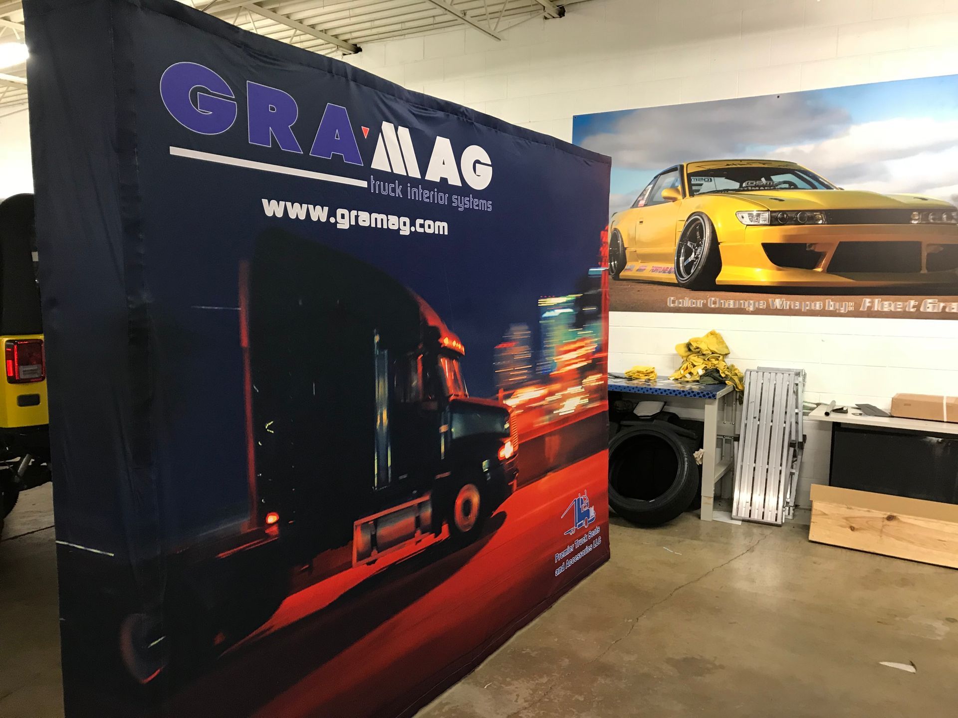 A semi-truck advertisement in a warehouse setting. A yellow car poster hangs in the background.
