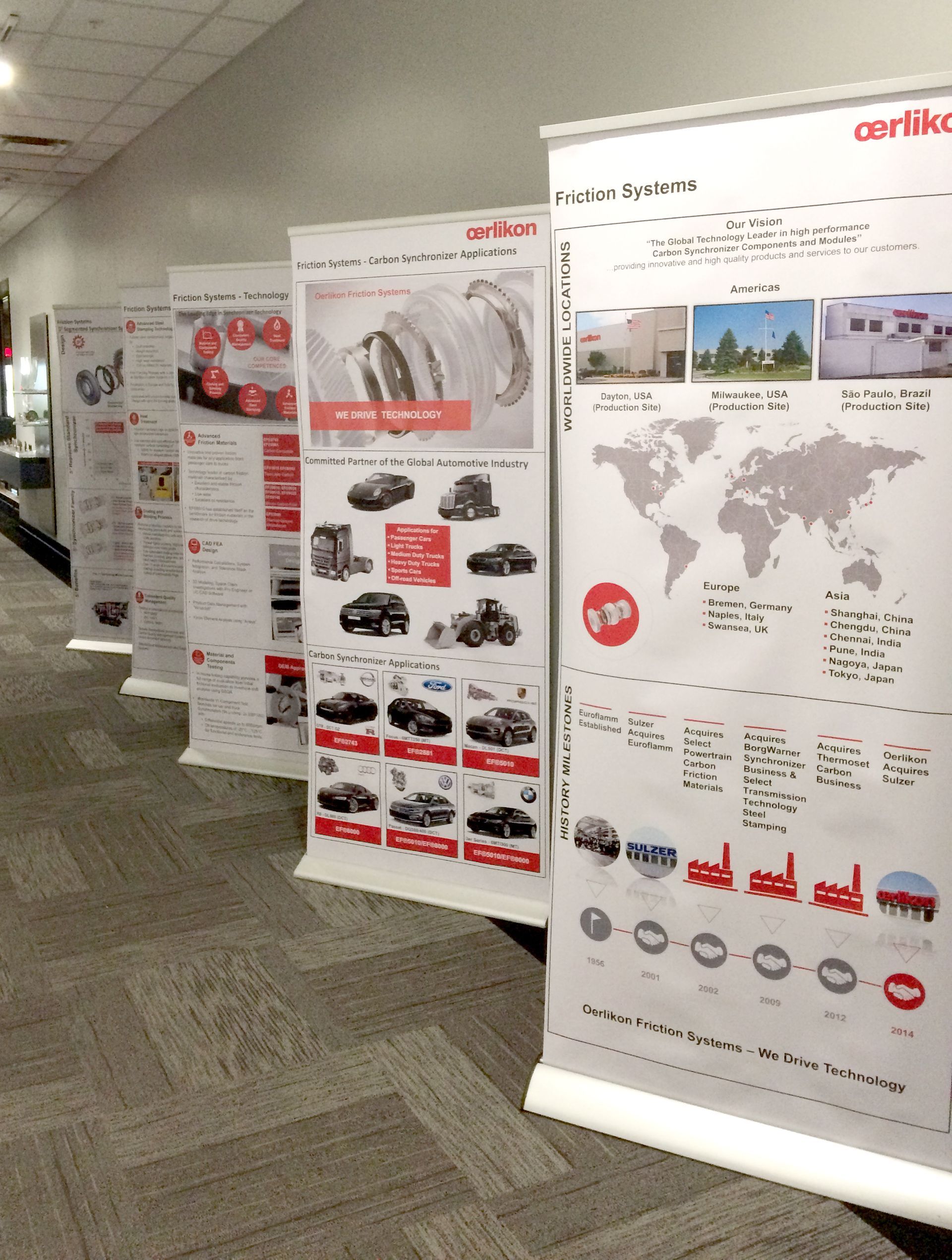 Row of informational pull-up banners in a room. Red and white graphics, showcasing products and company info.