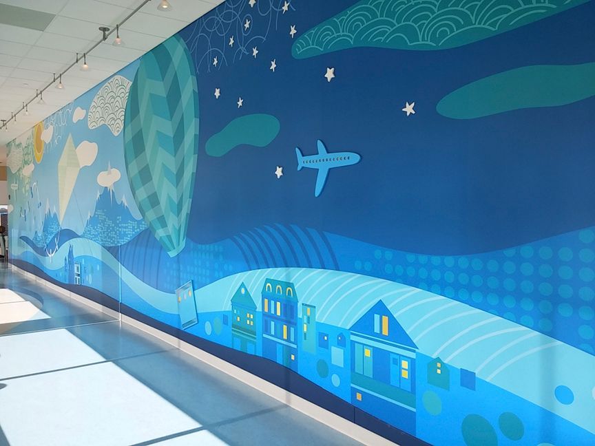 Mural of blue city and landscape with plane and stars, along a hallway.