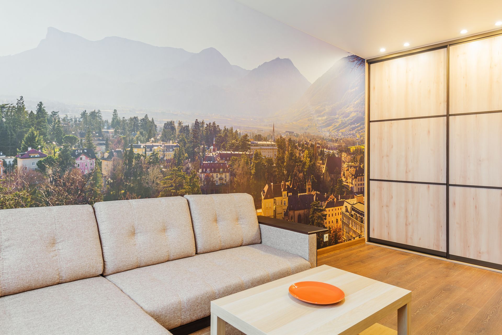 Beige sofa in a living room with cityscape mural and light wood sliding closet doors.