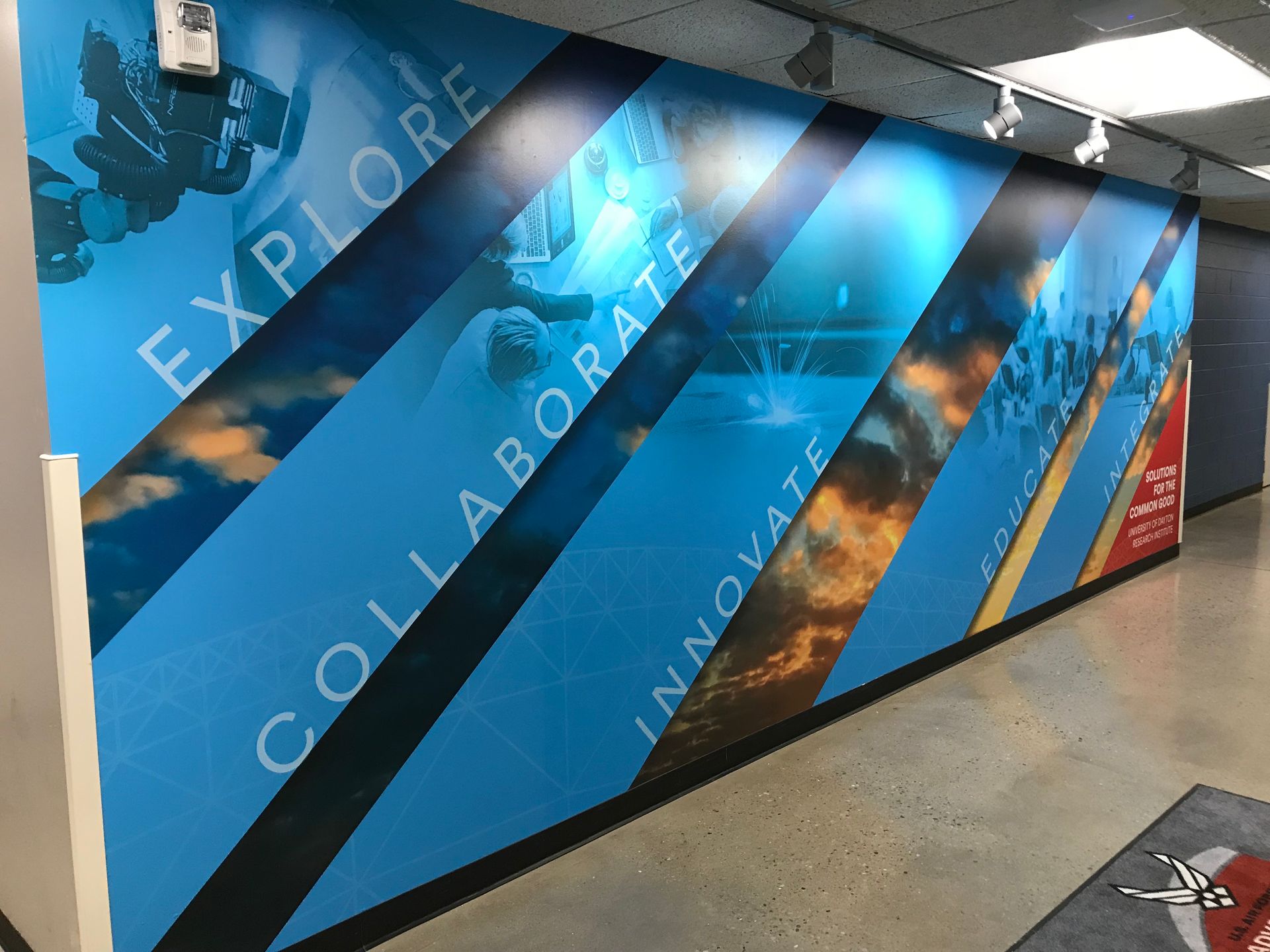 Blue wall mural with text: Explore, Collaborate, Innovate; hallway setting.