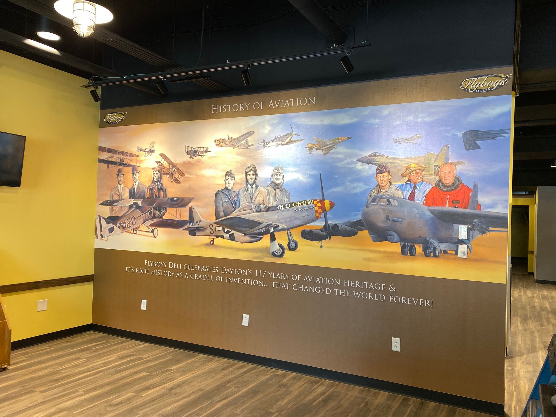 Mural depicting various aircraft and pilots, in a museum setting with yellow walls and wooden floor.