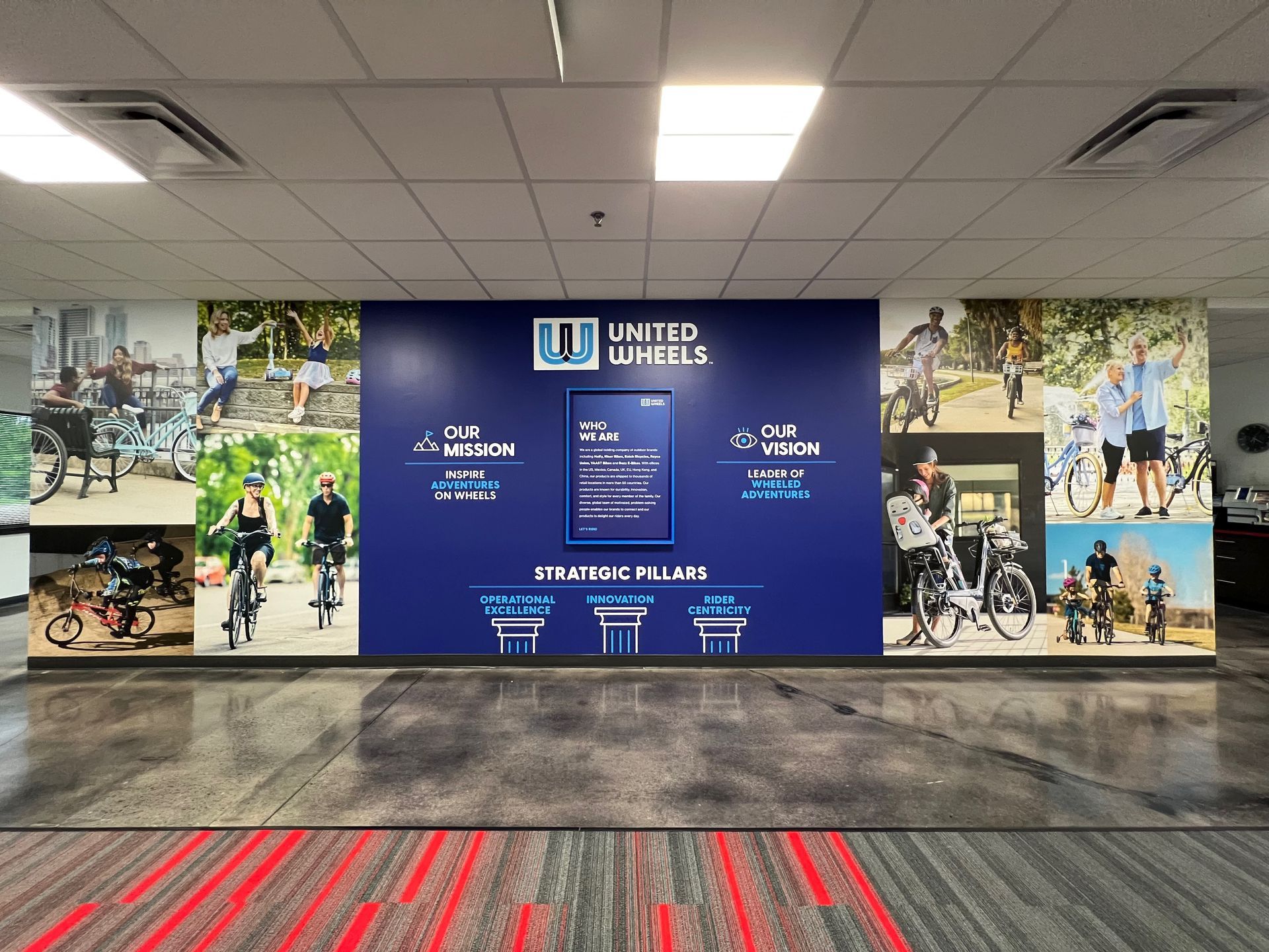 Office wall mural for United Wheels. Blue backdrop with logo, anniversary message, and people riding bikes.