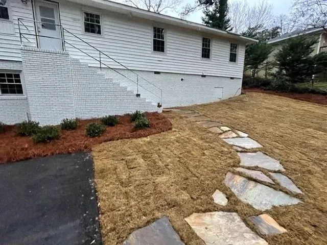 Side view of a white house with a brick staircase, new mulch, stone walkway, and fresh lawn.