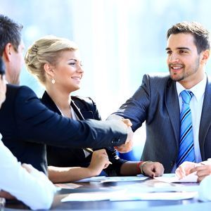 A group of people are sitting around a table shaking hands.