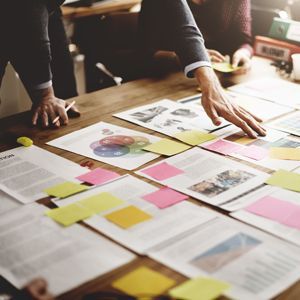 A group of people are sitting around a table with papers and sticky notes on it.
