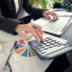 A woman is typing on a laptop and using a calculator.