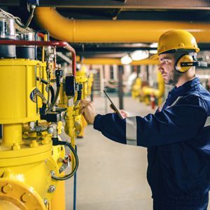 A man wearing a hard hat and ear muffs is working on a machine in a factory.