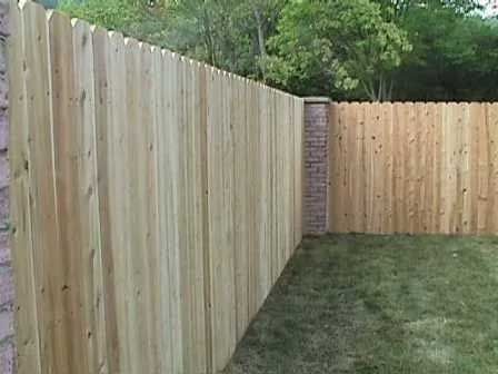 A wooden fence surrounds a brick wall in a backyard.