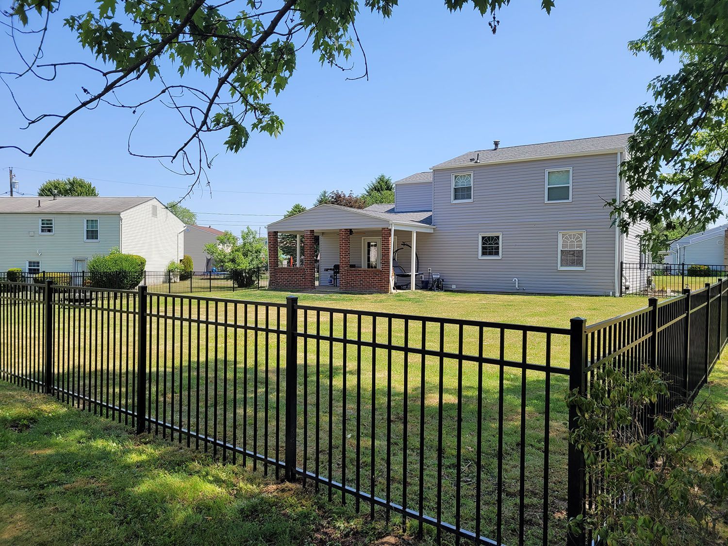 A black fence surrounds a yard with a house in the background.