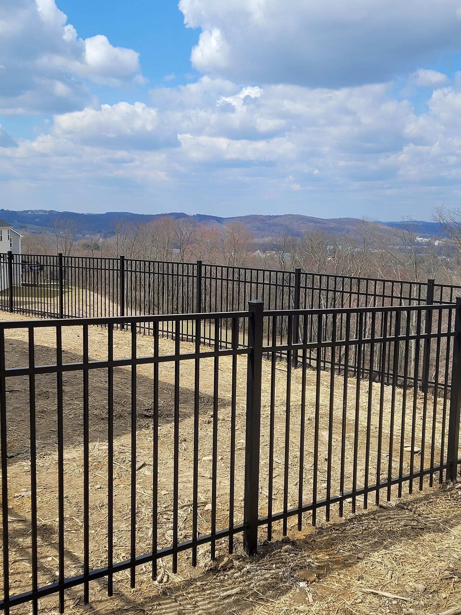 A black metal fence surrounds a dirt field with mountains in the background.