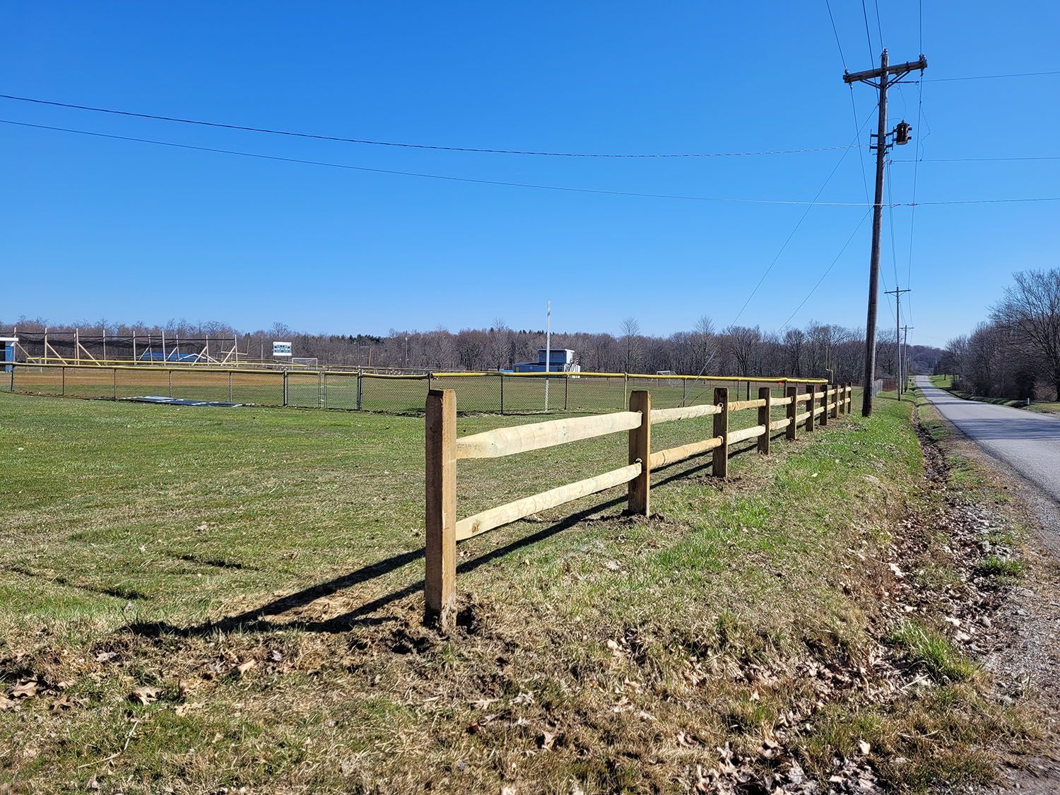 A wooden fence surrounds a grassy field next to a road.