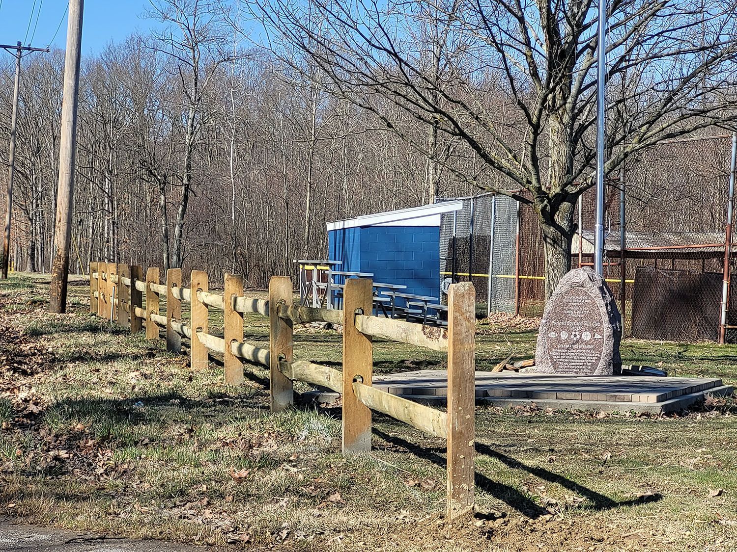 A wooden fence surrounds a field with a blue trailer in the background.