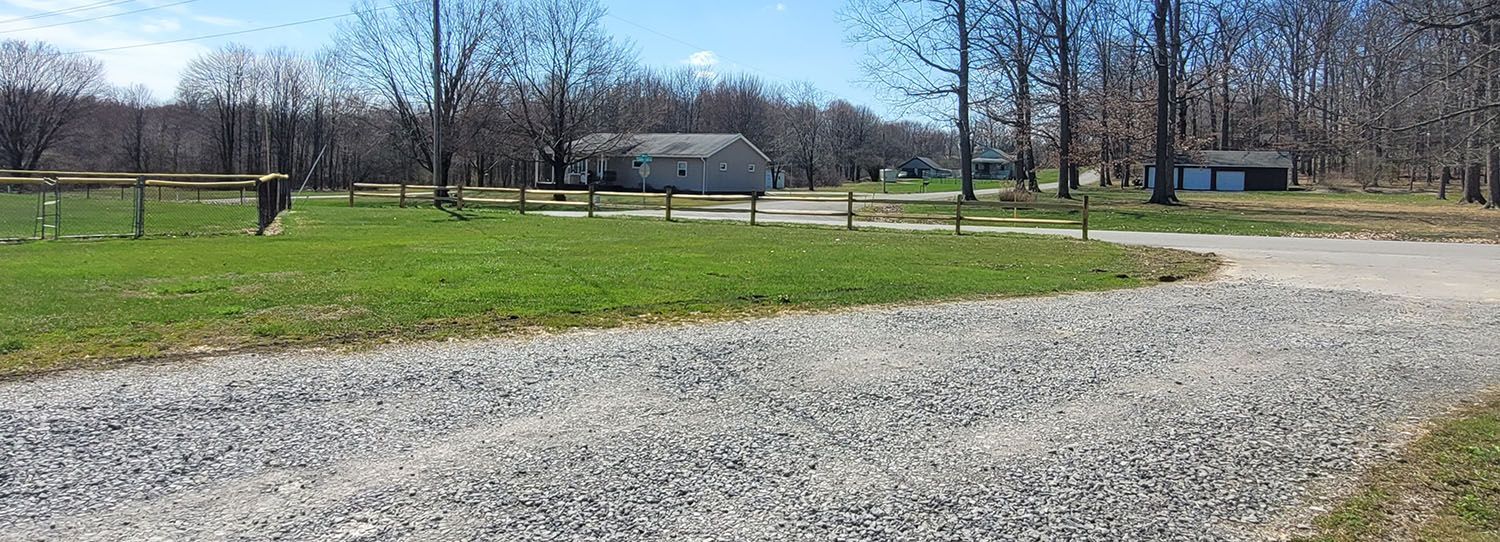 A gravel road going through a grassy field with trees in the background.