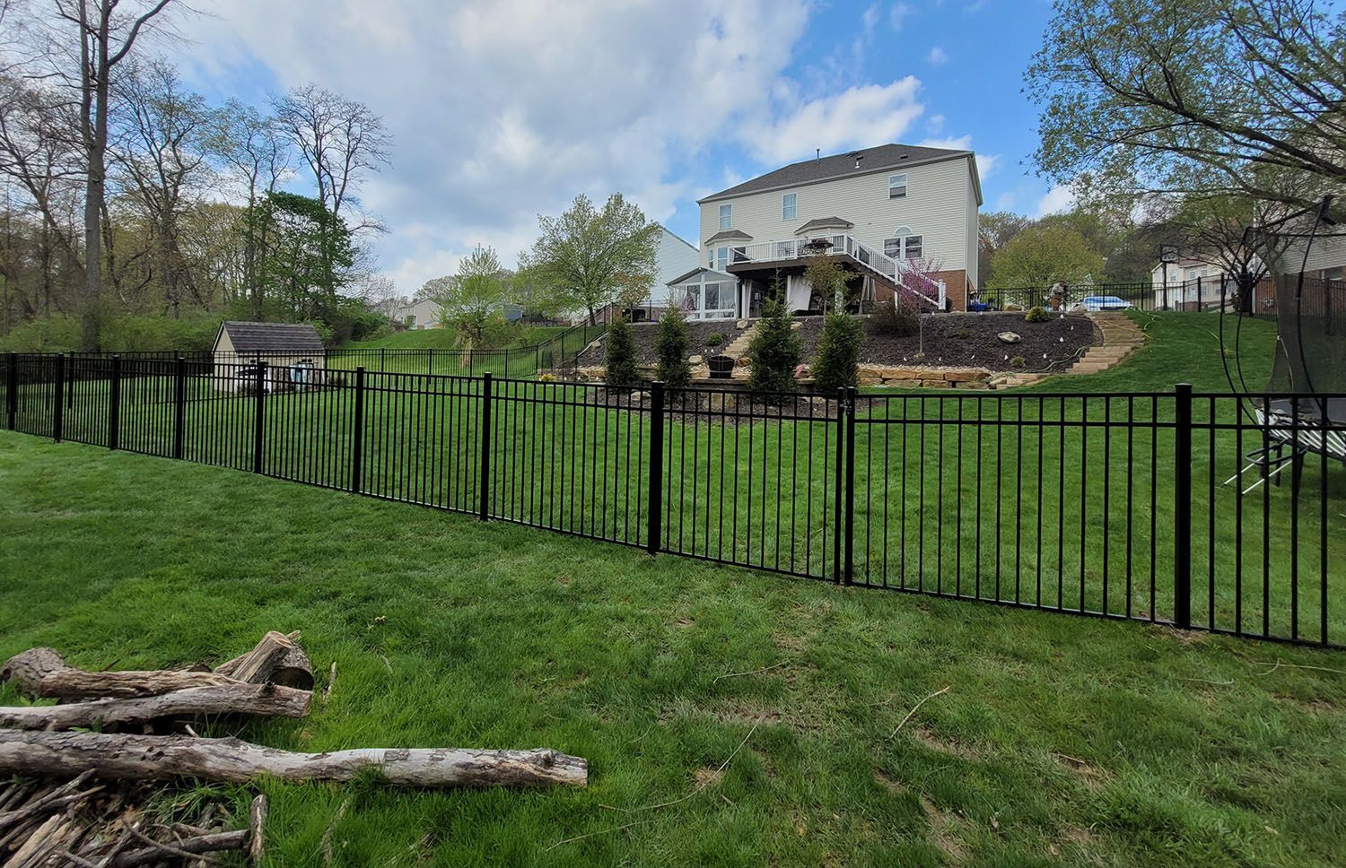 A black fence surrounds a lush green yard with a house in the background.