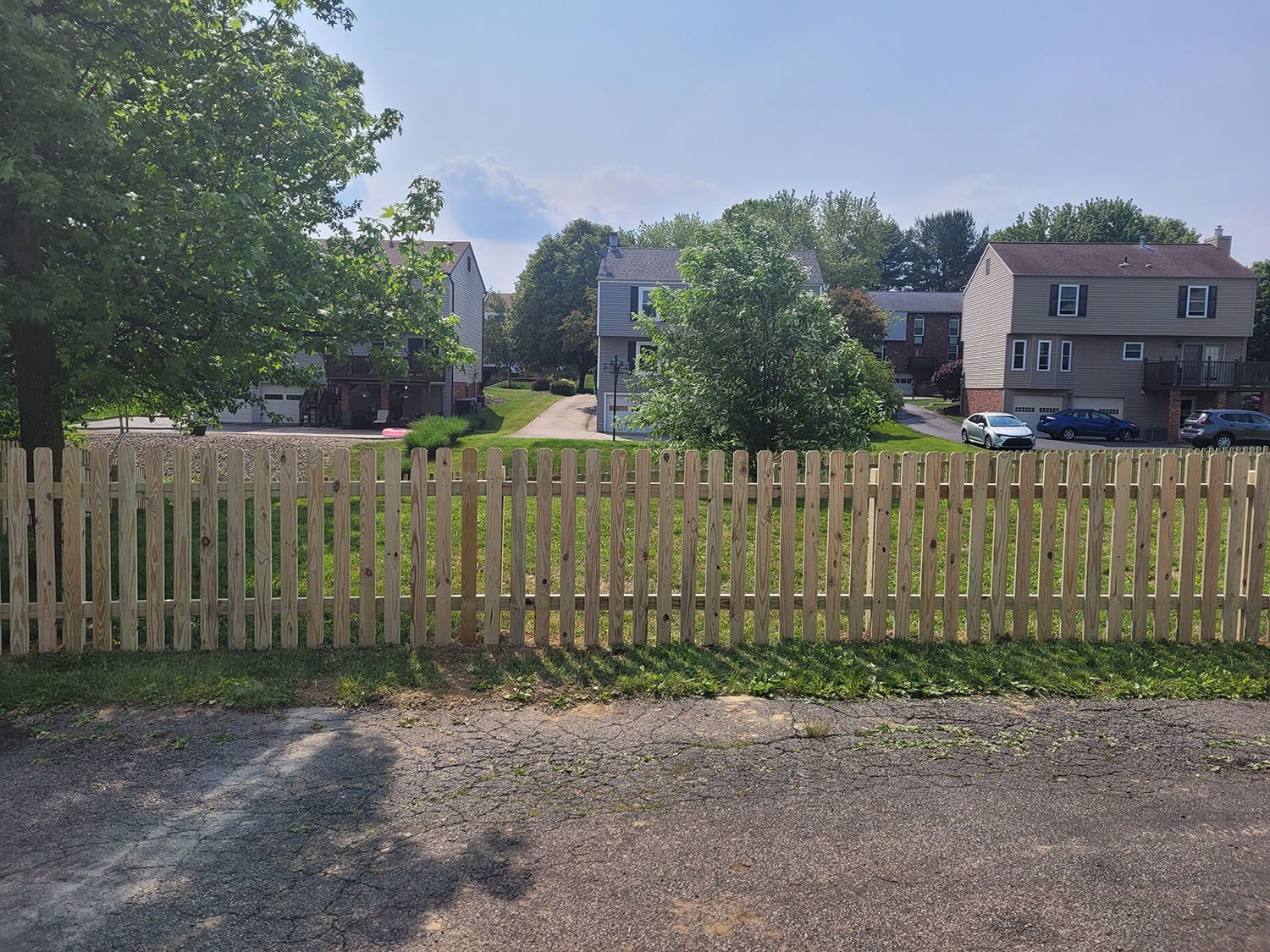 A wooden picket fence surrounds a residential area with houses in the background.