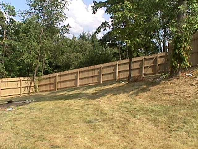 A wooden fence surrounds a grassy yard with trees in the background