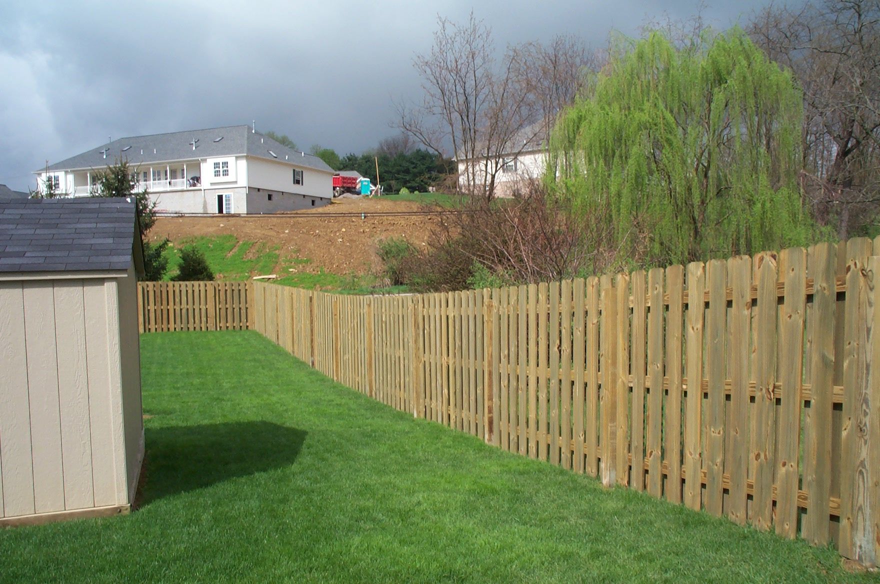 A wooden fence surrounds a lush green yard with houses in the background