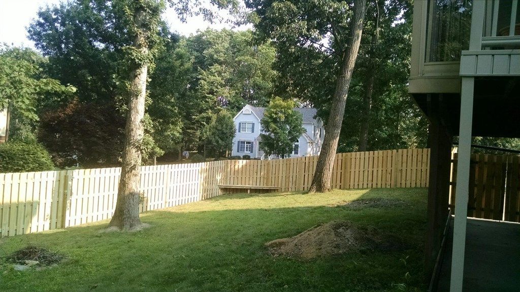 A backyard with a wooden fence and a house in the background