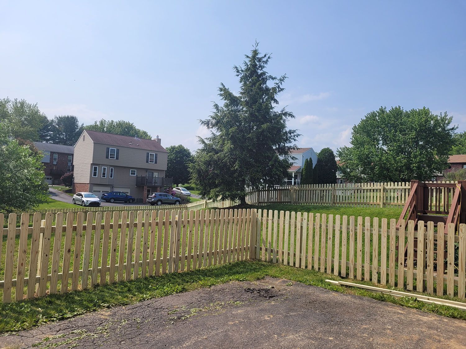 A wooden fence surrounds a grassy area with a house in the background.
