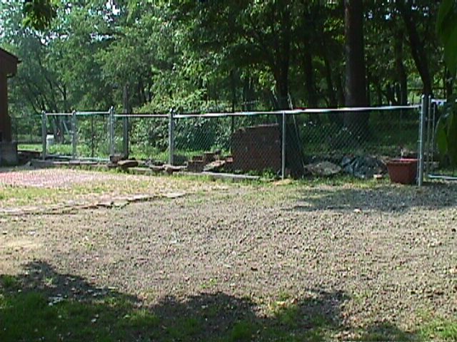 A chain link fence surrounds a dirt area with trees in the background