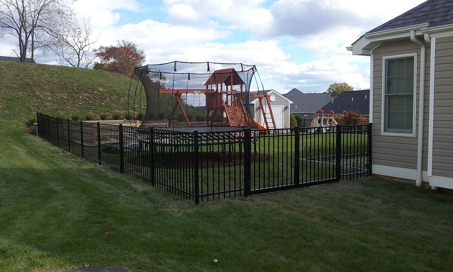 A house with a black fence and a playground in the backyard.