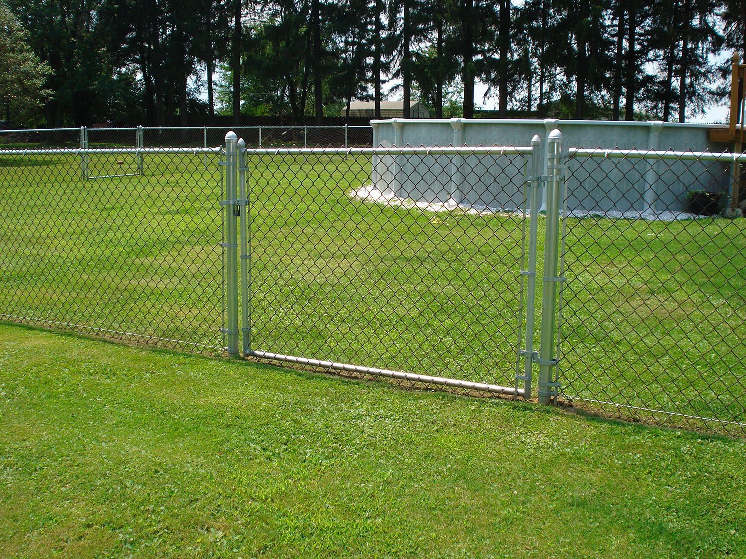 A chain link fence surrounds a lush green field with a pool in the background.