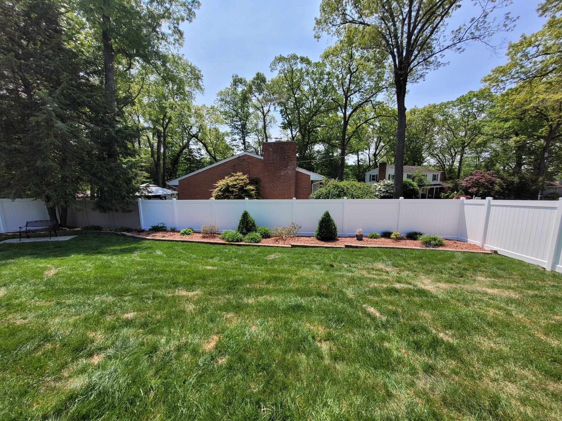 A backyard with a white fence and a lush green lawn.