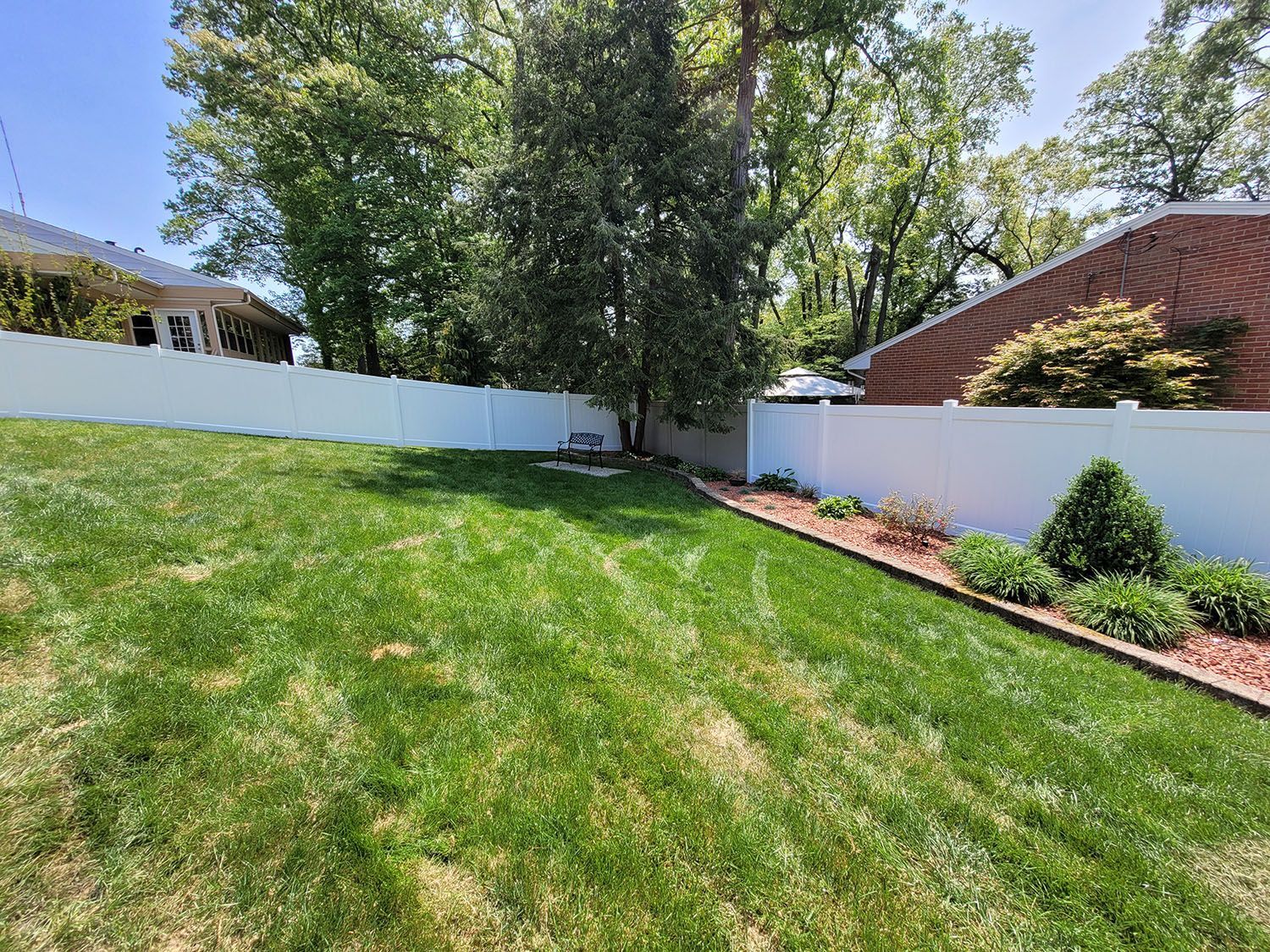 A backyard with a white fence and a lush green lawn.