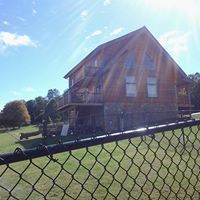 A large wooden house is behind a chain link fence.